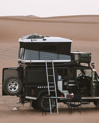 James Baroud Hartschalen-Dachzelt Grand Raid schwarz montiert auf einem Offroad-Fahrzeug. Dachzelt ist aufgebaut. Mit Leiter Zustieg. Gepäck auf dem Dach.
