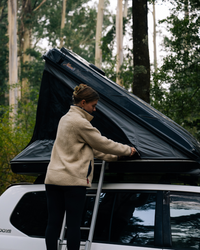 James Baroud Hartschalen-Dachzelt  Discovery montiert auf einem Offroad-Fahrzeug beim Campen. Eine Frau macht die Fenster zu.