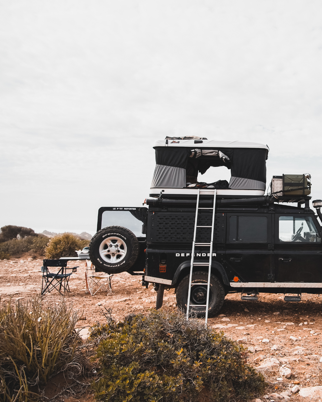 James Baroud Hartschalen-Dachzelt Grand Raid schwarz montiert auf einem Offroad-Fahrzeug. Dachzelt ist aufgebaut. Fenster offen. Mit Leiter Zustieg. Gepäck auf dem Dach.