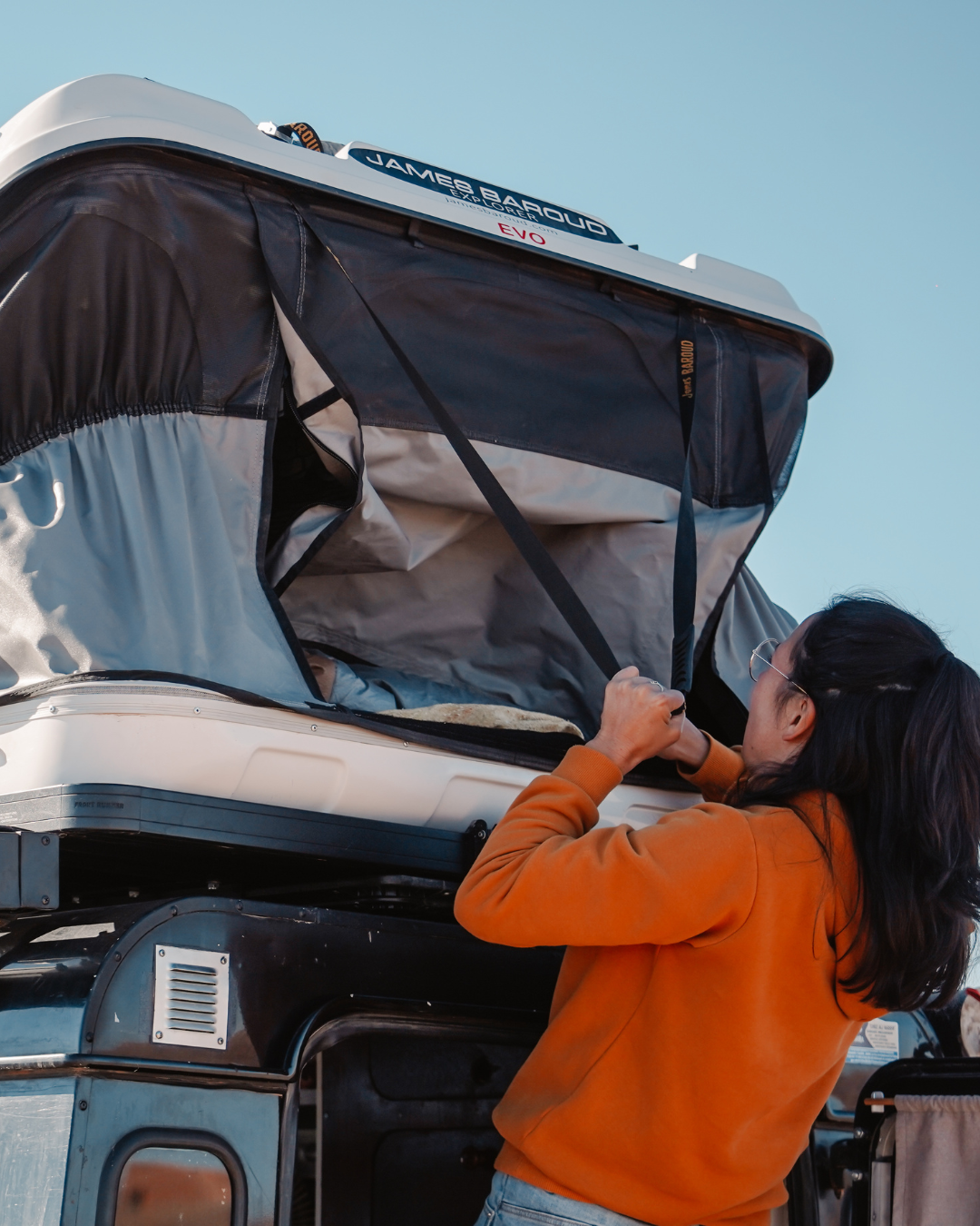 James Baroud Hartschalen-Dachzelt Grand Raid schwarz montiert auf einem Offroad-Fahrzeug. Dachzelt wird eingeklappt. Gurt zum runterziehen.