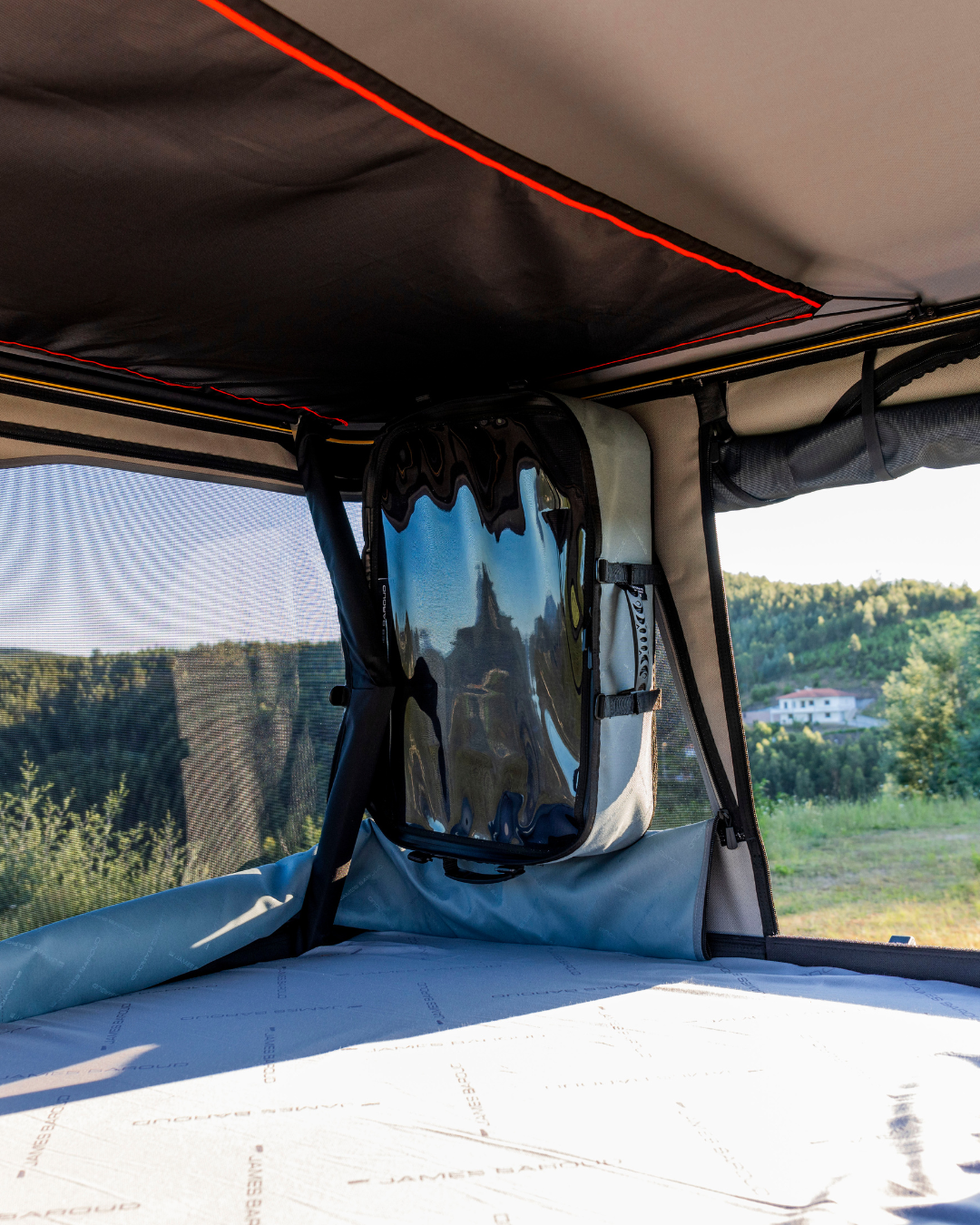 James Baroud Hartschalen-Dachzelt Odyssey Magma. Bild aus dem Innenraum mit geöffneten Fenster und montierter James Baroud Aufbewahrungsbox an der Wandseite.