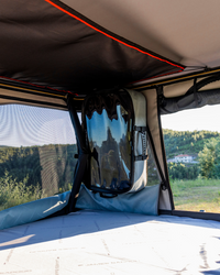 James Baroud Hartschalen-Dachzelt Odyssey Magma. Bild aus dem Innenraum mit geöffneten Fenster und montierter James Baroud Aufbewahrungsbox an der Wandseite.