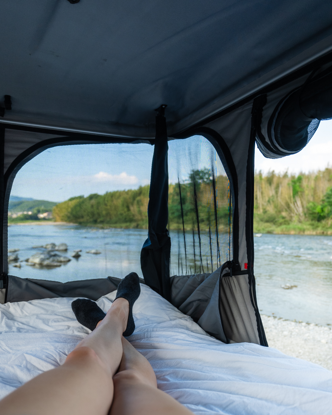 James Baroud Hartschalen-Dachzelt. Blick aus dem inneren durch ein großes Fenster und dem Stoff auf einen Fluss.