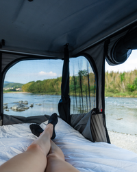 James Baroud Hartschalen-Dachzelt. Blick aus dem inneren durch ein großes Fenster und dem Stoff auf einen Fluss.