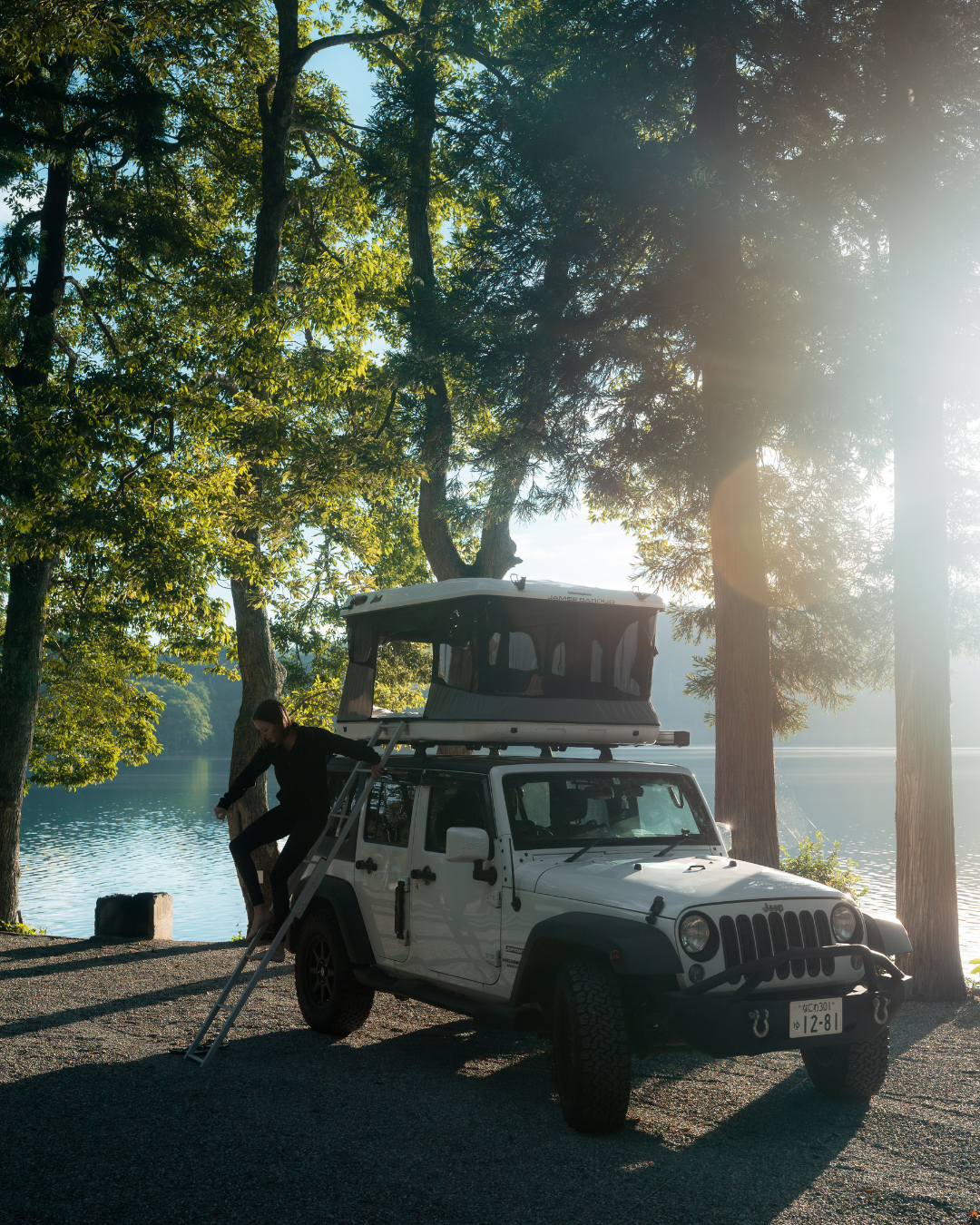 James Baroud Hartschalen-Dachzelt  montiert auf einem Offroad-Fahrzeug beim Campen. Ein Mann klettert über die Leiter runter.