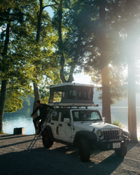 James Baroud Hartschalen-Dachzelt  montiert auf einem Offroad-Fahrzeug beim Campen. Ein Mann klettert über die Leiter runter.
