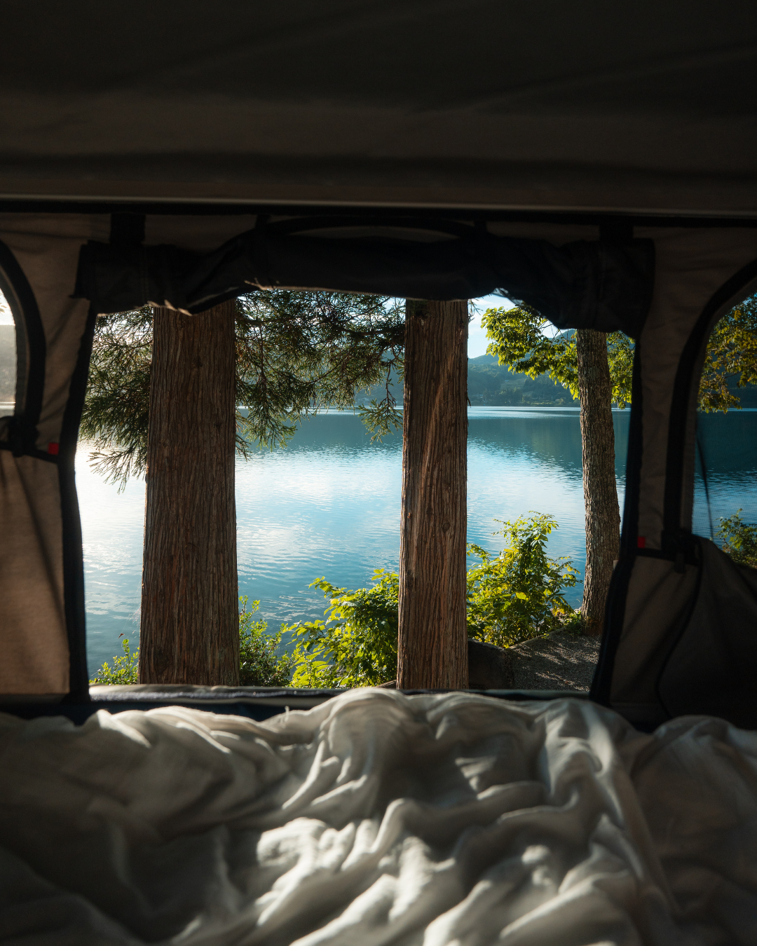 James Baroud Hartschalen-Dachzelt. Blick aus dem inneren durch ein großes Fenster auf einen See