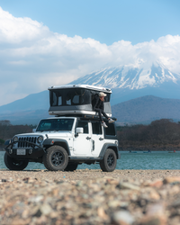James Baroud Hartschalen-Dachzelt Evasion weiß montiert auf einem Offroad-Fahrzeug. Dachzelt ist aufgebaut. Frau sitzt am Einstieg.