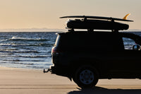 James Baroud Hartschalen-Dachzelt Odyssey montiert auf einem Fahrzeug am Meer mit Surfbrett auf den Querträgern.