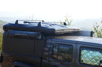 James Baroud Hartschalen-Dachzelt Odyssey schwarz geschlossen montiert auf einem Offroad-Fahrzeug. Mit montierten Querträger am dem Dachzelt und montierter Duschkabine